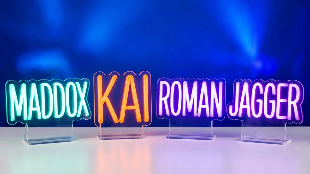 Glowing neon name signs in teal, orange and purple showing the cool boy names Maddox, Kai, Roman and Jagger on a white table